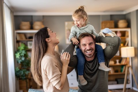 © iStock-2231459517/Milan Markovic Glückliches Paar mit Kind auf den Schultern