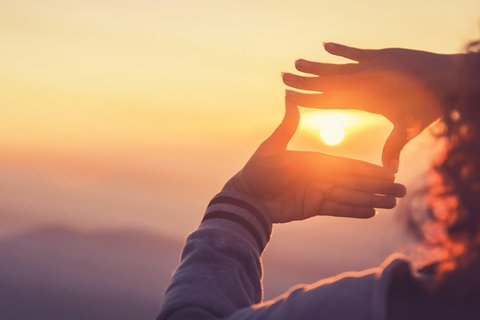 Eine Frau macht einen Rahmen um die Sonne mit ihren Händen im Sonnenaufgang
