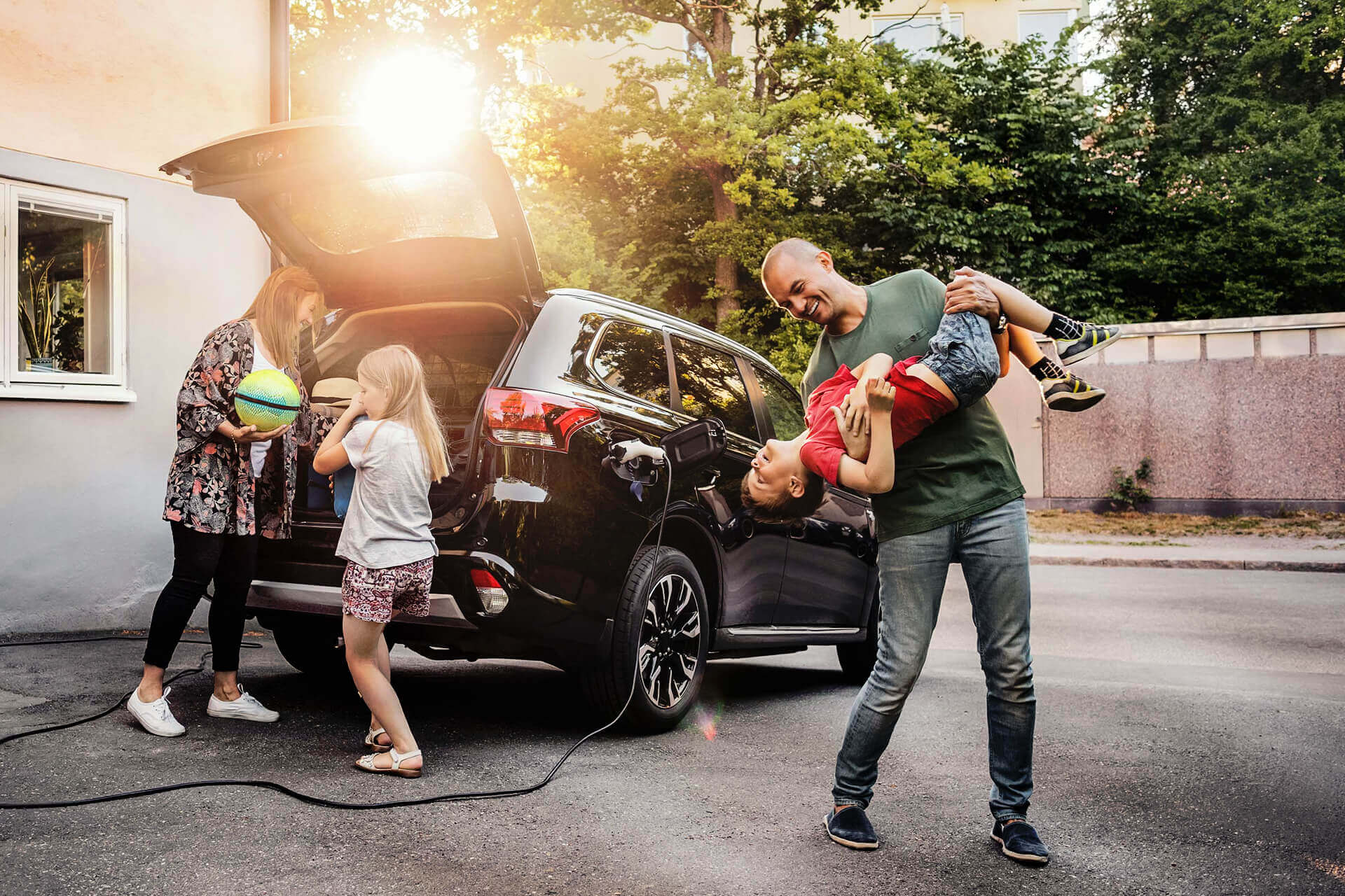 Vater und Sohn mit Frau und Mädchen stehen an Ihrem Elektro-Auto, das gerade mit Strom aufgeladen wird.